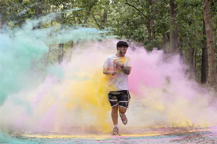 A student runs through clouds of green, pink and yellow colored powder during a color run