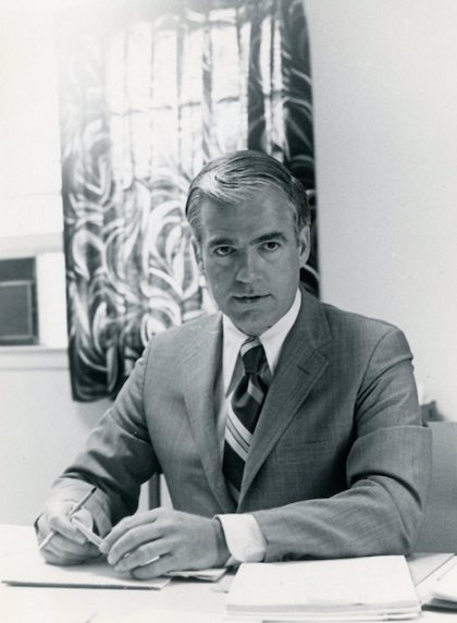 President Richard Bjork in black and white, sitting at a table with a stack of papers