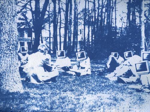 Students sitting on the on the grass listening to a lecture with computer monitors for heads